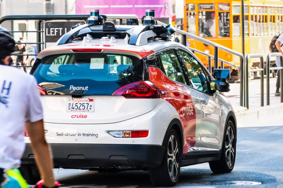 Self-driving white and red Cruise vehicle (Chevy Bolt body) in San Francisco with cyclist following behind